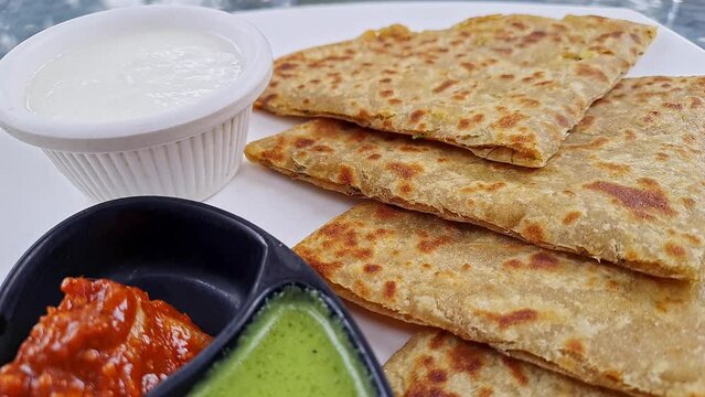 Pan shot of Indian famous food aloo paratha or flatbread served with yogurt and chutney