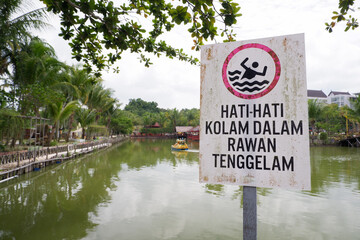 warning board with the words Hati hati kolam dalam rawan tenggelam in English, be careful, deep...