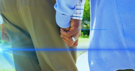 Image of light moving over midsection of senior couple walking holding hands