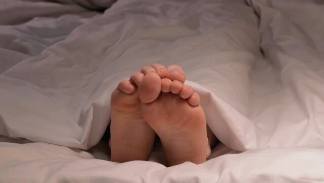 female legs and toes itch and scabies in the evening in bed on a sheet under a blanket. Woman girl with bare feet foot with fungus under stress sleeps on a bed in a bedroom at night in a hotel