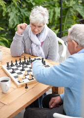 Chess, strategy and senior couple thinking while playing a board game in the backyard or bonding...