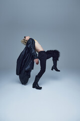 Shirtless man in black pants and heeled boots bending backward in artistic dance move against grey...