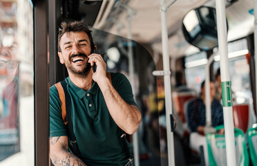 Portrait of a young happy man using public transportation and talking on the phone.