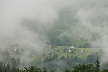 Dense fog in the mountains, through which the houses and the village are barely visible.