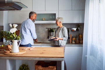 A lovely senior couple smiling at each other while doing the dishes together and standing in the kitchen
