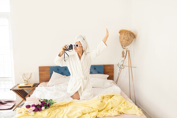 Fototapeta na wymiar stylish Asian woman in bathrobe and sunglasses, towel and restro camera having fun in bed