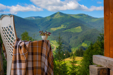 An armchair with a blanket and a bouquet of flowers and a magnificent view from the terrace of the green mountains in the sunlight. summer holiday and magnificent view