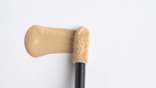 A smear of foundation cream or concealer with a brush on a white background, macro. Liquid foundation or bb cream beige color smudge. Texture of cosmetic liquid foundation