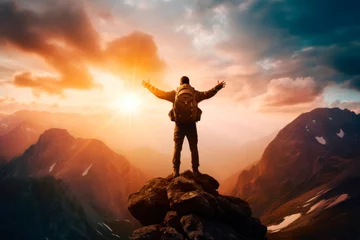 Wandaufkleber A young male tourist with a large backpack with outstretched arms looks at the sunset in the mountains © Elena