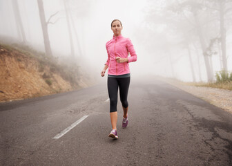 Fototapeta premium Nature, sports and woman running in fog on mountain road for race, marathon or competition training. Fitness, exercise and female athlete with cardio workout in misty outdoor woods or forest.