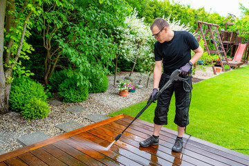 man cleaning terrace with a power washer - high water pressure cleaner on wooden terrace surface - 741415051