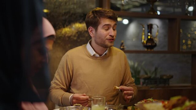 Young Caucasian Man Similing While Looking at His Family Members and Having a Conversation at a Restaurant During Ramadan