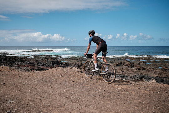 Man cyclist is riding a gravel bicycle a gravel road with beautiful view on Atlantic ocean on Tenerife, Canary Islands, Spain. Sport motivation. Cycling training outdoors in Spain. Cycling adventure.