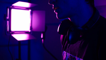 Young man with headphones in a music studio with a purple spotlight in the background 