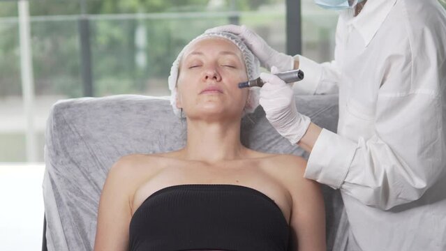 A cosmetologist does a dermapen procedure on a woman's face
