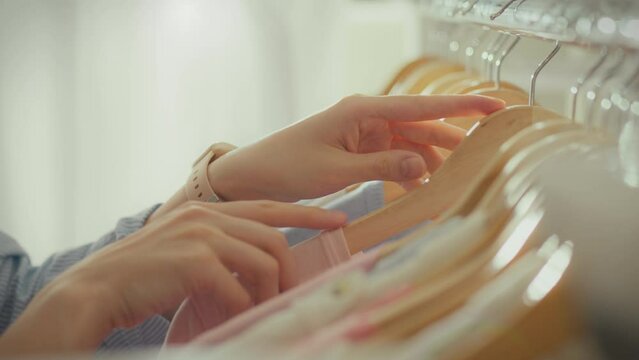 In a bright designer clothing boutique, a model woman easily inspects the clothes on the racks. An independent woman follows fashion trends when choosing and purchasing goods