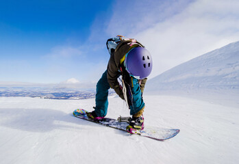 A person in winter gear snowboarding down a steep slope covered in fresh white snow. Girl preparing...
