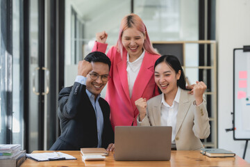 Triumphant asian business team with raised fists celebrating success at the office. Corporate achievement and teamwork concept.