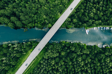 Aerial view of bridge road with car over blue river and green woods in Finland