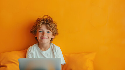 A young boy is sitting on a bed, focused on a laptop computer in front of him. He appears to be engaged in online learning or educational lessons