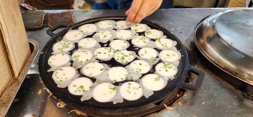 Khanom Krok Pan or Thai Coconut Pudding Pan filled with flour. The vendor is making khanom krok Traditional Thai desserts and sprinkling chopped green onions into the uncooked dough. Thai sweetmeat.
 - obrazy, fototapety, plakaty