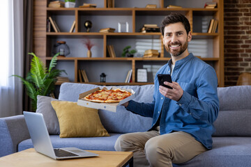 Casual man smiling with pizza box and smartphone on sofa, home comfort