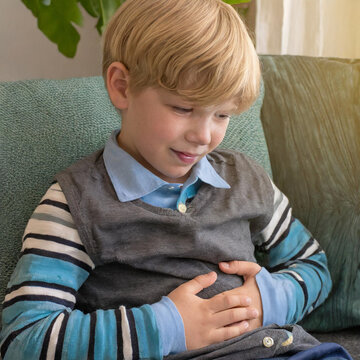 Ein blonder Junge h&auml;lt die H&auml;nde vor dem Bauch, weil er Bauchschmerzen hat