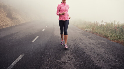 Running, legs and woman on road outdoor in forest, park or woods for exercise in winter. Morning, fog and person with fitness training and healthy workout on path in mountain countryside with nature