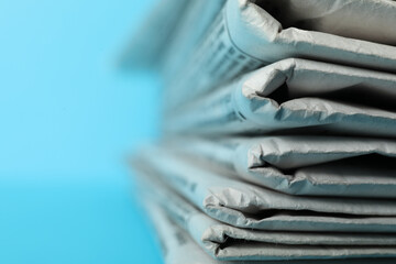Stack of newspapers on light blue background, closeup. Journalist's work