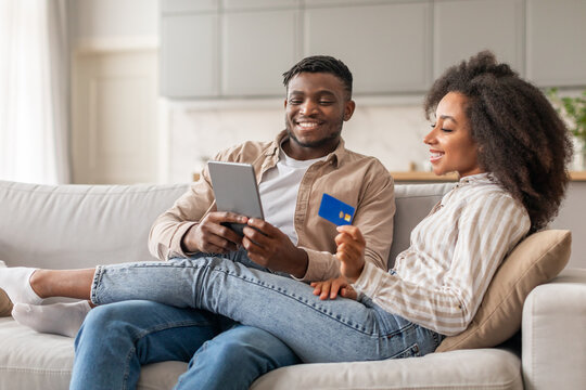African couple holding credit card exploring webstore on tablet indoor