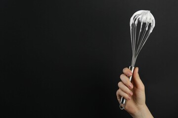 Woman holding whisk with whipped cream on black background, closeup. Space for text