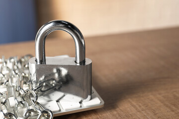 Cyber security. Keyboard with padlock and chain on wooden table, closeup. Space for text