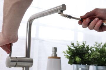 Plumber repairing faucet with spanner indoors, closeup