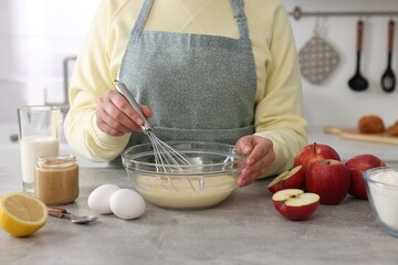 Woman whisking eggs in bowl at grey table indoors, closeup