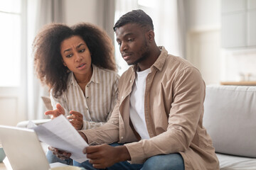 Concerned black married couple solving problems with papers at home