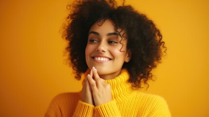 A cheerful woman in a yellow sweater smiling and resting her hand on her chin. Suitable for lifestyle and fashion concepts - obrazy, fototapety, plakaty