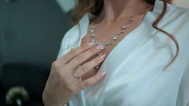 a beautiful young bride in a white dress with an open neckline hangs pearl jewelry on her neck and strokes her body, morning preparations before the wedding ceremony