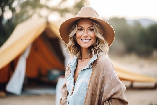 Portrait of beautiful young woman in hat and coat standing near tent
