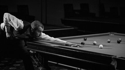 Stylishly dressed guy confidently playing in snooker game. Advertisement image of trendy billiards lounge or bar. Black and white. Concept of billiards sport, gambling, hobby, leisure, game