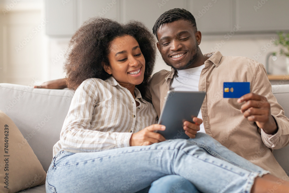 Wall mural black couple enjoying shopping on tablet holding credit card indoors