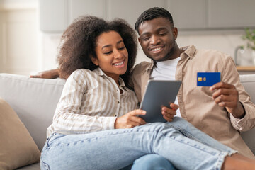 black couple enjoying shopping on tablet holding credit card indoors