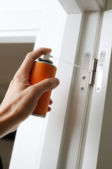 man sprays some lubricating oil on the hinge of a door - 741497289