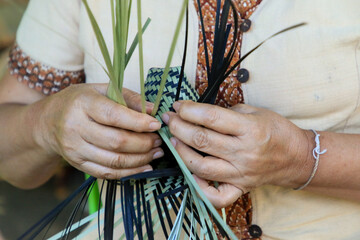 A Thai woman´s hand is weaving an ancestral basket case from bamboo. People are demonstrating...