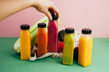 Fruit and vegetable smoothies in transparent plastic bottles. Red, green, yellow smoothie in the hand on a pink-green background with avocado, apples and celery. The concept of healthy eating