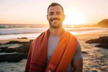 Portrait of a smiling man wrapped in a red shawl on the beach at sunset