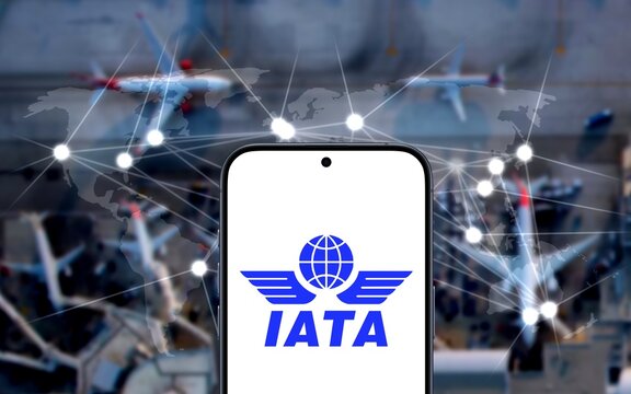 IATA Logo is shown on a modern smartphone, International Air Transport Association, in the background an airport with airplanes and world map with connections, aviation, regulations 