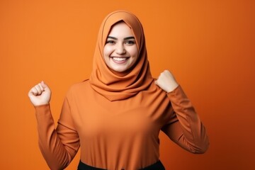 Beautiful young Muslim woman smiling confidently. Professional. Traditional looking camera pointing sideways on orange background.