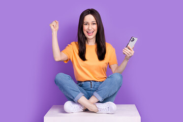 Photo of successful mature business woman with smartphone sit podium and celebrating winning auction isolated on violet color background