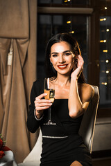 Luxurious woman in a black dress has dinner in a restaurant with flowers and a glass of champagne.Romantic dinner.International Women's Day concept
