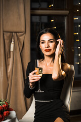 Luxurious woman in a black dress has dinner in a restaurant with flowers and a glass of champagne.Romantic dinner.International Women's Day concept
